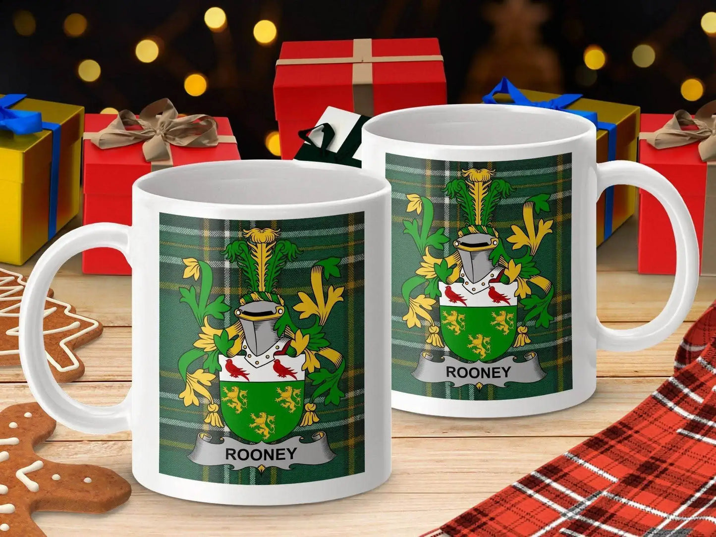 White ceramic mugs with green Rooney family crest and plaid background, surrounded by Christmas gifts and gingerbread