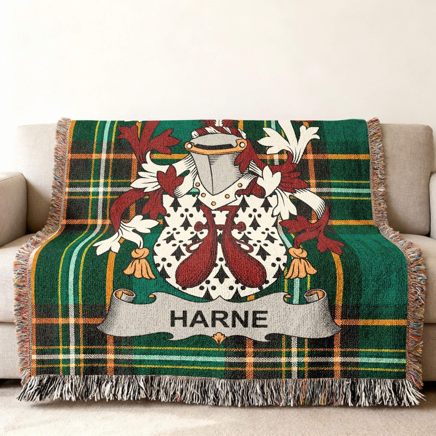 Green plaid throw blanket with HARNE crest and tasseled fringe on a sofa.