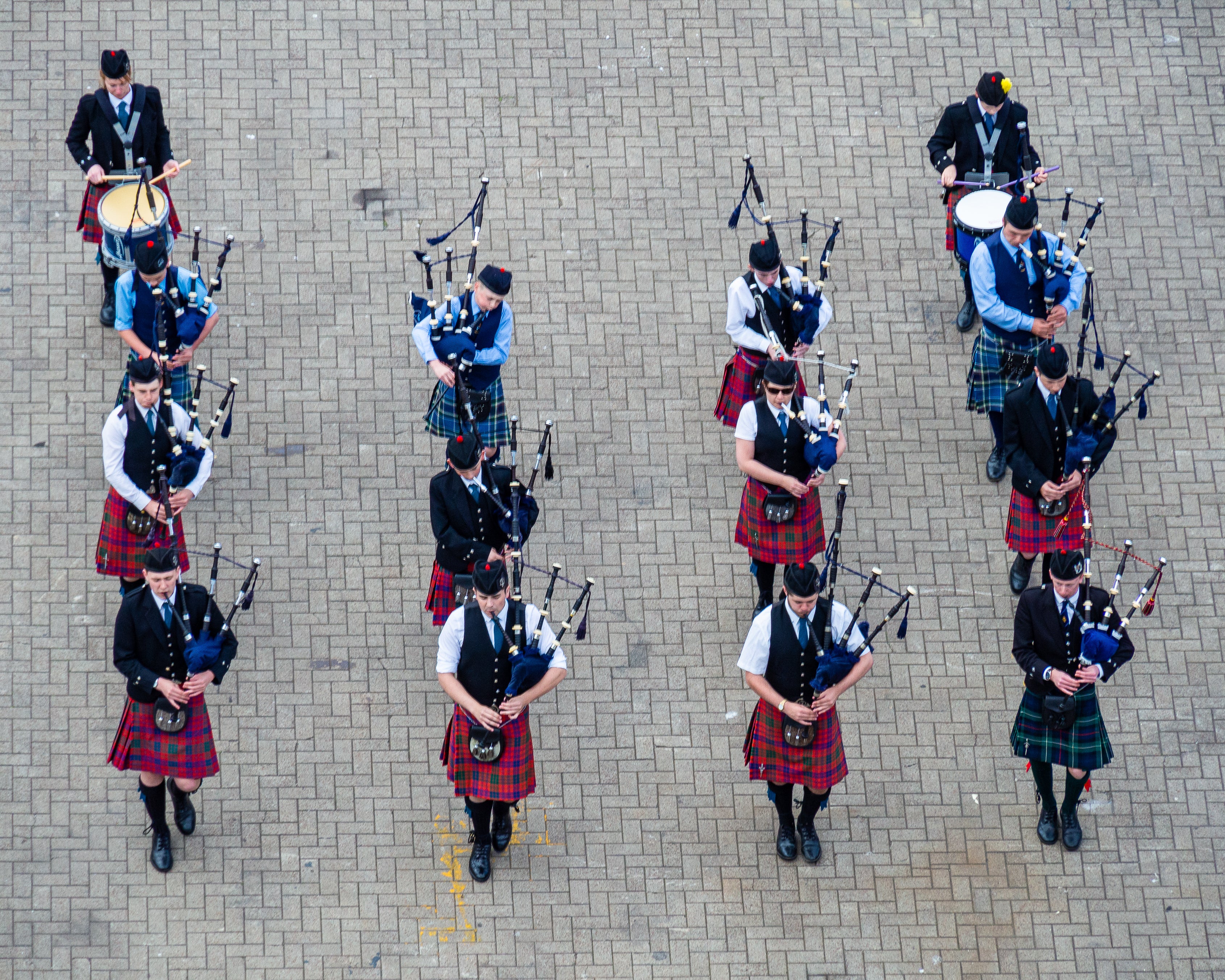 Twelve pipers in full Highland tartan dress performing at Invergordon in Scotland, the vivid clan colours of their kilts representing the natural dye traditions that gave each Scottish clan tartan its distinctive regional identity