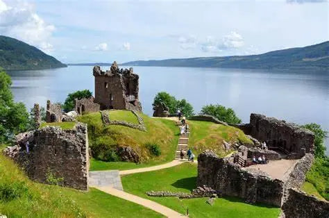 Scenic ruins of Urquhart Castle overlooking Loch Ness with green hills and a winding path