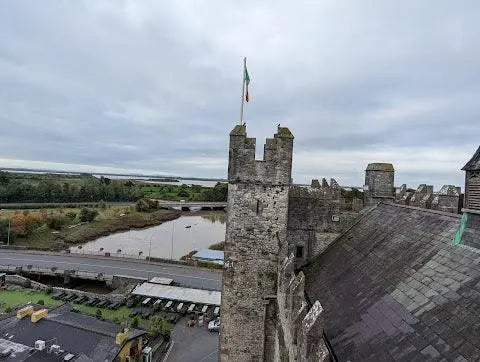 Historic stone castle tower with Irish flag overlooking a river and cloudy sky in Ireland