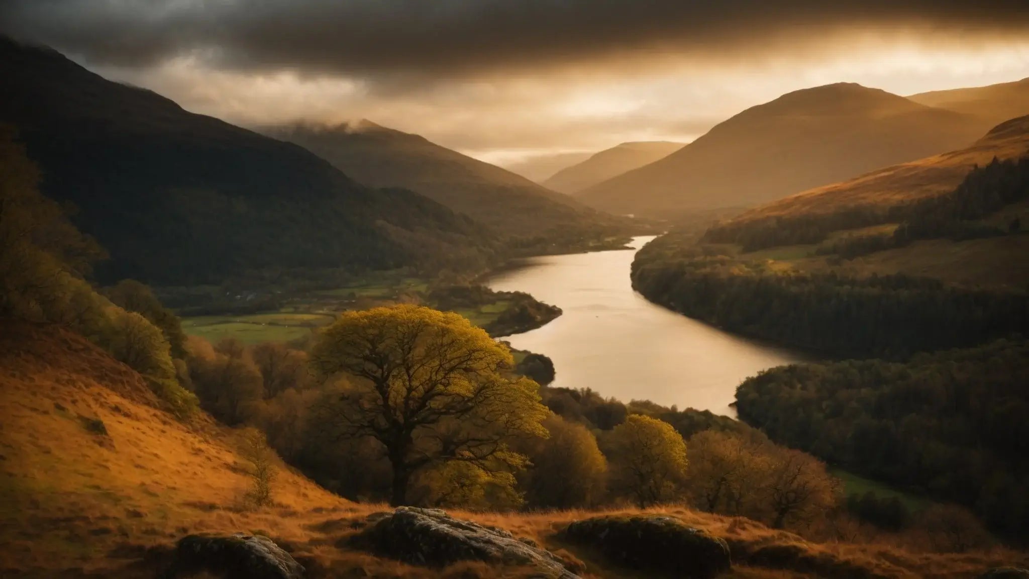 Scenic view of a winding river through a golden valley with hills under dramatic cloudy sky