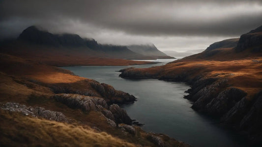 Moody Scottish Highlands landscape with rocky shores, calm water, and mist-covered mountains under cloudy sky