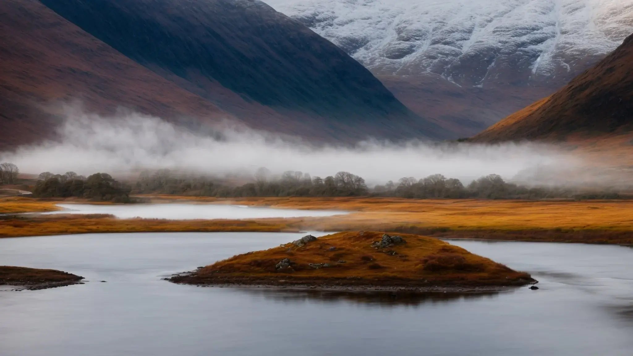 Misty autumn Highland valley with calm river, golden grass, and snow-capped mountains in the background