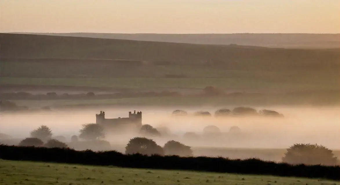 Scottish castle ruins surrounded by mist and rolling green hills at sunrise