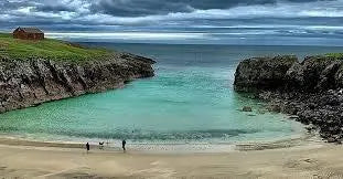 Tranquil Scottish coastal bay with turquoise water, sandy beach, cliffs, and a small cabin on grassy hill