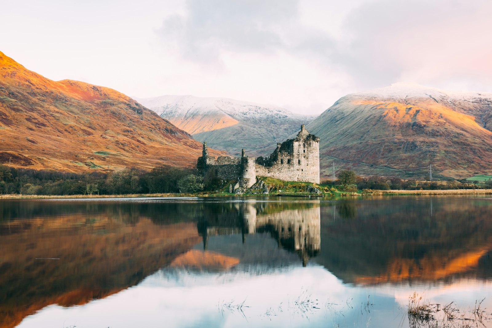 Medieval castle ruin reflected in still water in the Scottish Highlands, built by Norman families who arrived in Scotland in the twelfth century
