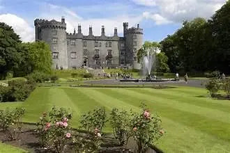 Historic stone castle with towers, manicured gardens, fountain, and blue sky background