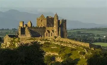 Ancient stone castle ruins on a hill with green fields and mountains in the background