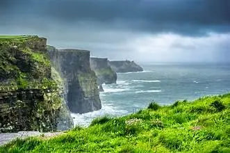 Scenic view of cliffs with lush green grass overlooking a stormy ocean under cloudy skies