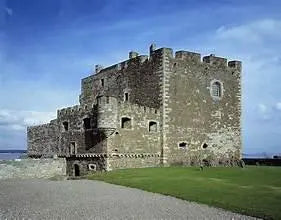 Historic stone castle with fortified walls on grassy coastline under blue sky