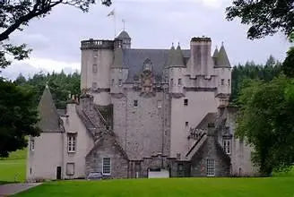 Historic Scottish castle with stone walls and turrets surrounded by green trees and lawn