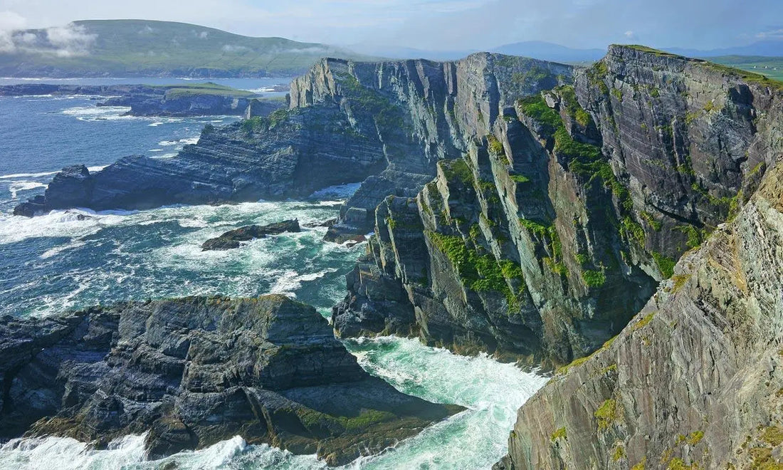 Dramatic coastal cliffs with green vegetation and waves crashing on rocks at Ring of Kerry, Ireland