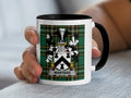 White mug with black rim and handle displaying the "Warters" family crest on a tartan background.