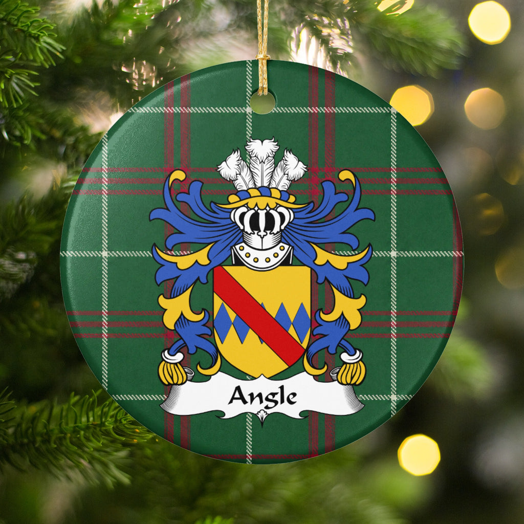 Angle family crest and surname on a round Welsh national tartan ornament, hanging by a gold cord among Christmas tree branches and warm golden lights.