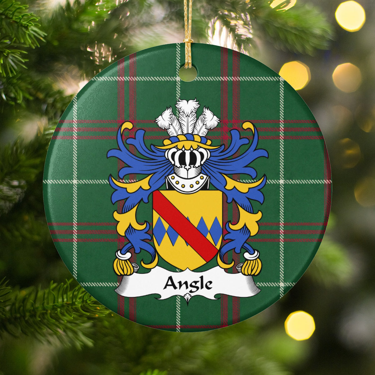 Angle family crest and surname on a round Welsh national tartan ornament, hanging by a gold cord among Christmas tree branches and warm golden lights.