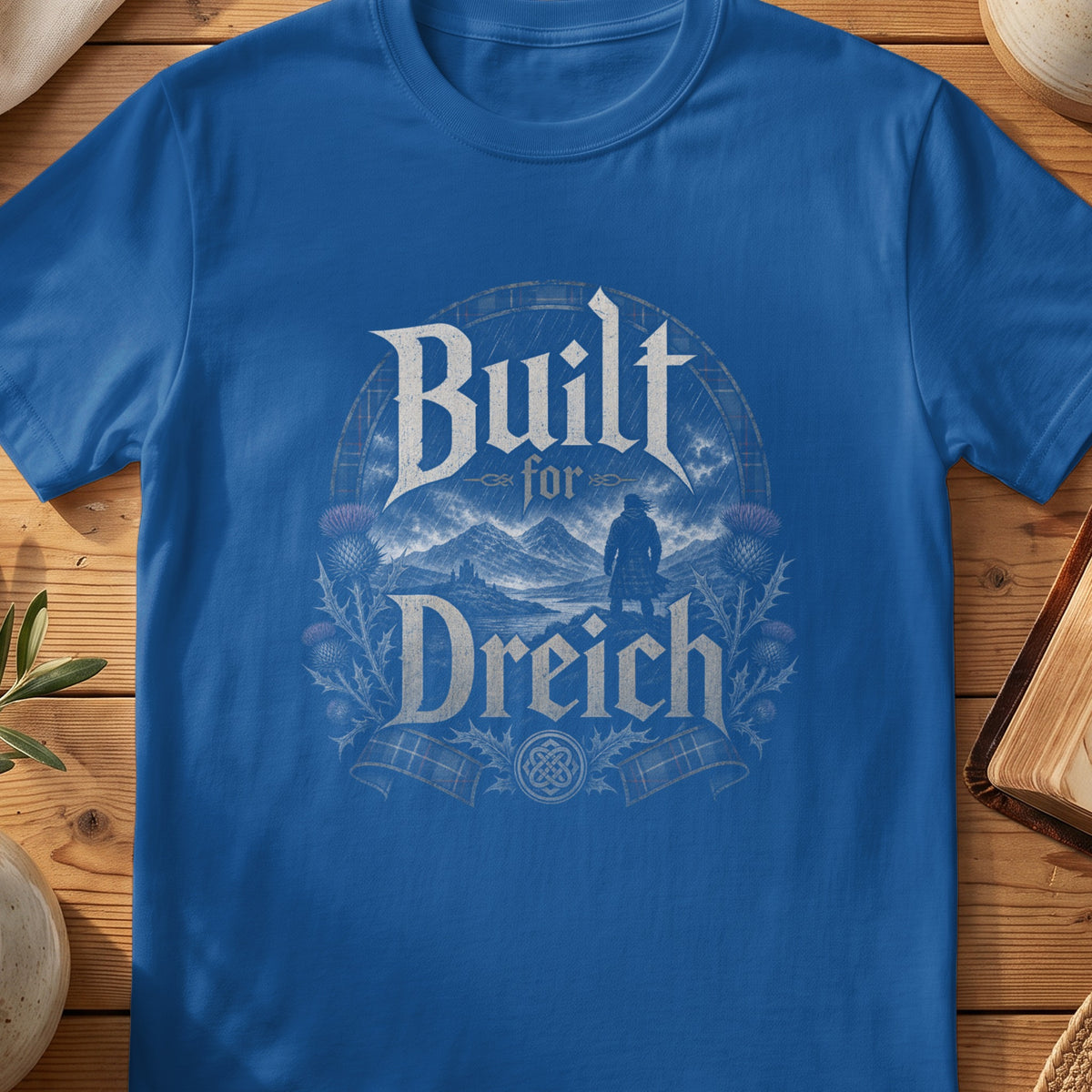 Blue t-shirt with "Built for Dreich" text over a Scottish highland landscape.