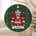 Catharne ornament hanging from a pale wooden branch; three white goat heads around a scalloped white band with leafy sprigs and red berries on a red shield on Welsh national tartan.