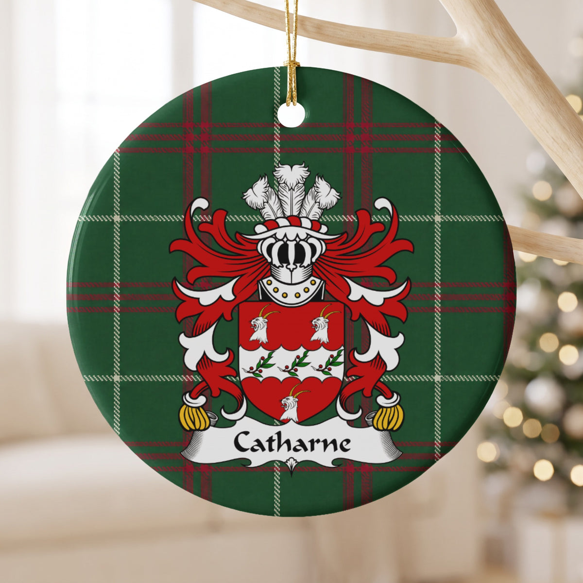 Catharne ornament hanging from a pale wooden branch; three white goat heads around a scalloped white band with leafy sprigs and red berries on a red shield on Welsh national tartan.