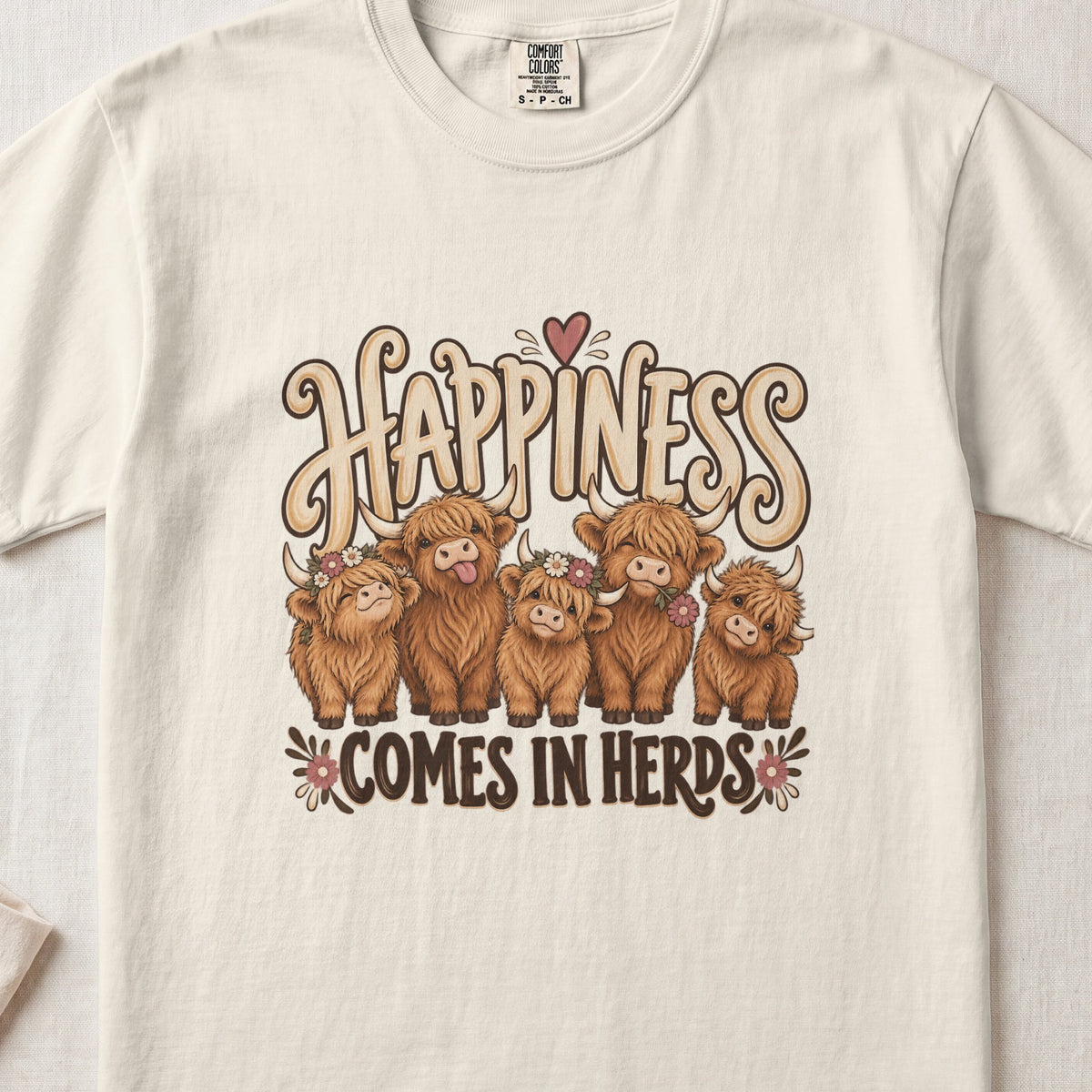 Happiness Comes in Herds Highland cow design on an Ivory Comfort Colors 1717 T-shirt, flat lay