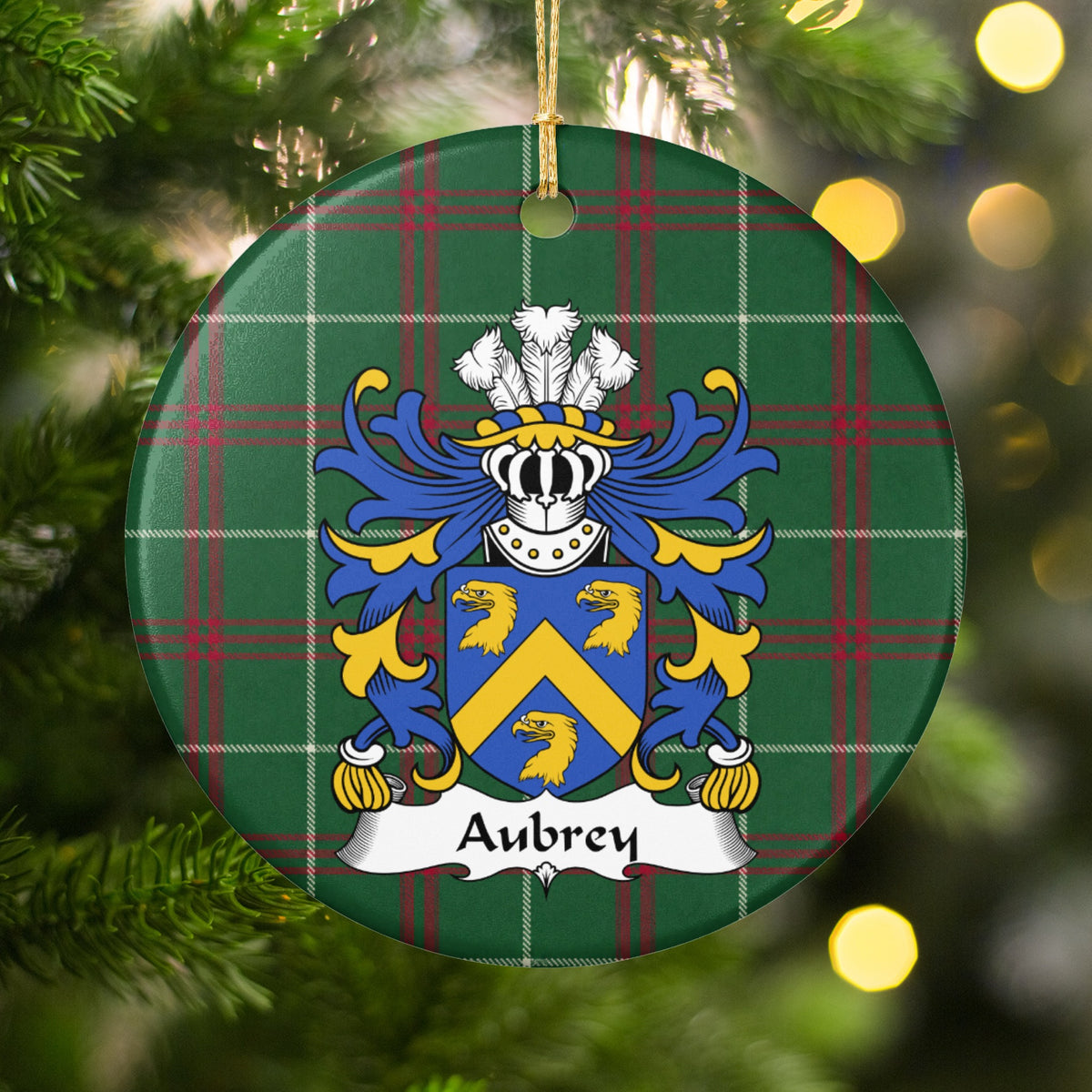 Aubrey ornament among Christmas tree branches and warm lights; three gold eagle heads and a gold chevron on a blue shield on Welsh national tartan.