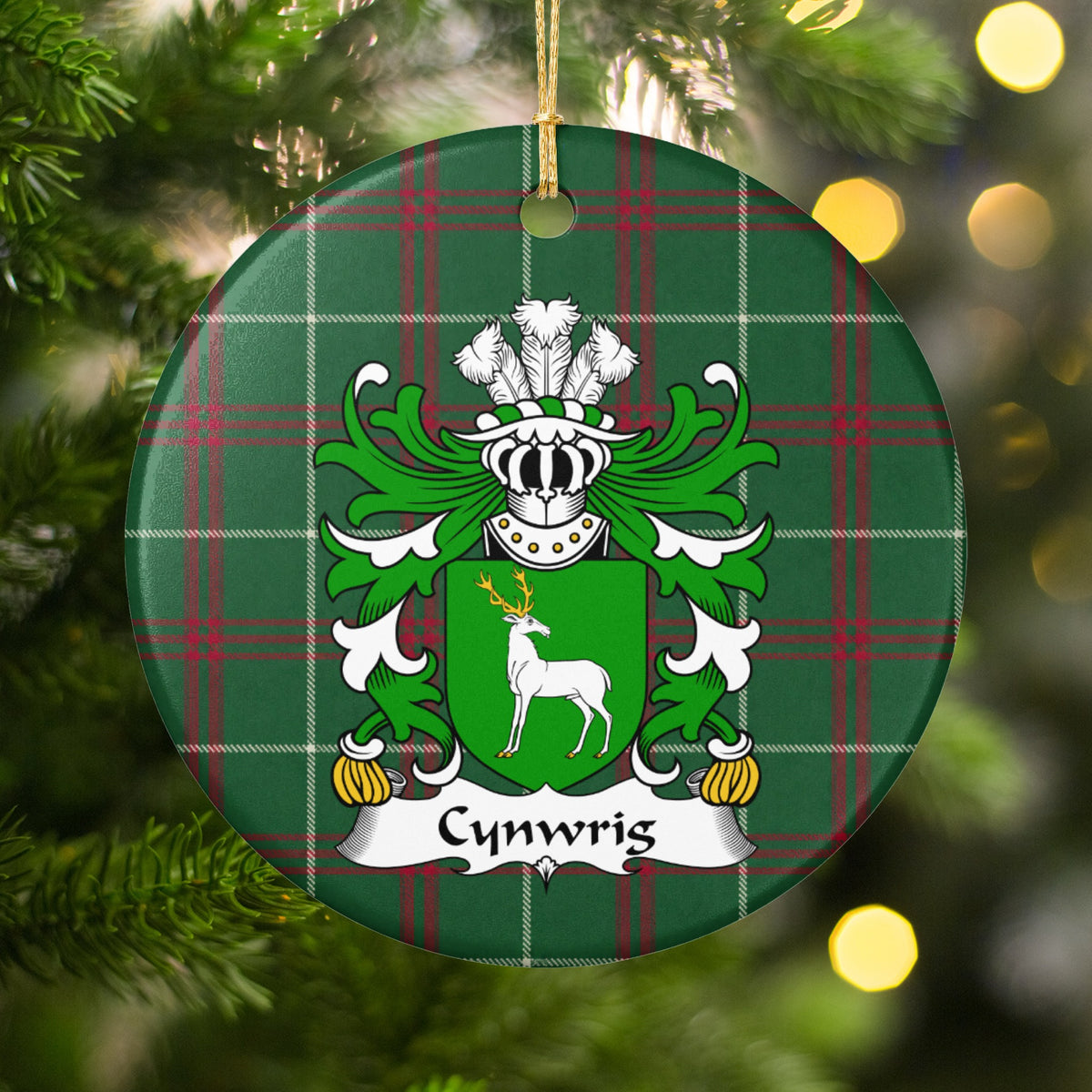 Cynwrig Style 2 ornament hanging among Christmas tree branches and warm lights; a white stag with gold antlers on a green shield on Welsh national tartan.
