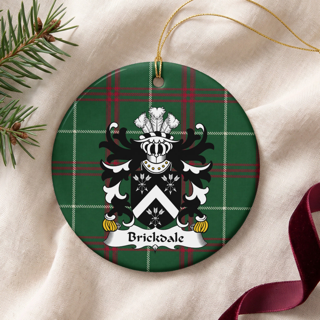 Brickdale ornament on cream fabric with gold string, evergreen and burgundy ribbon; a white chevron between three white arrow bundles on black on Welsh national tartan.