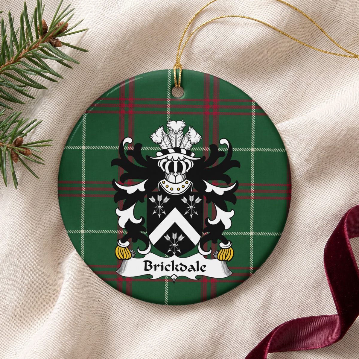 Brickdale ornament on cream fabric with gold string, evergreen and burgundy ribbon; a white chevron between three white arrow bundles on black on Welsh national tartan.