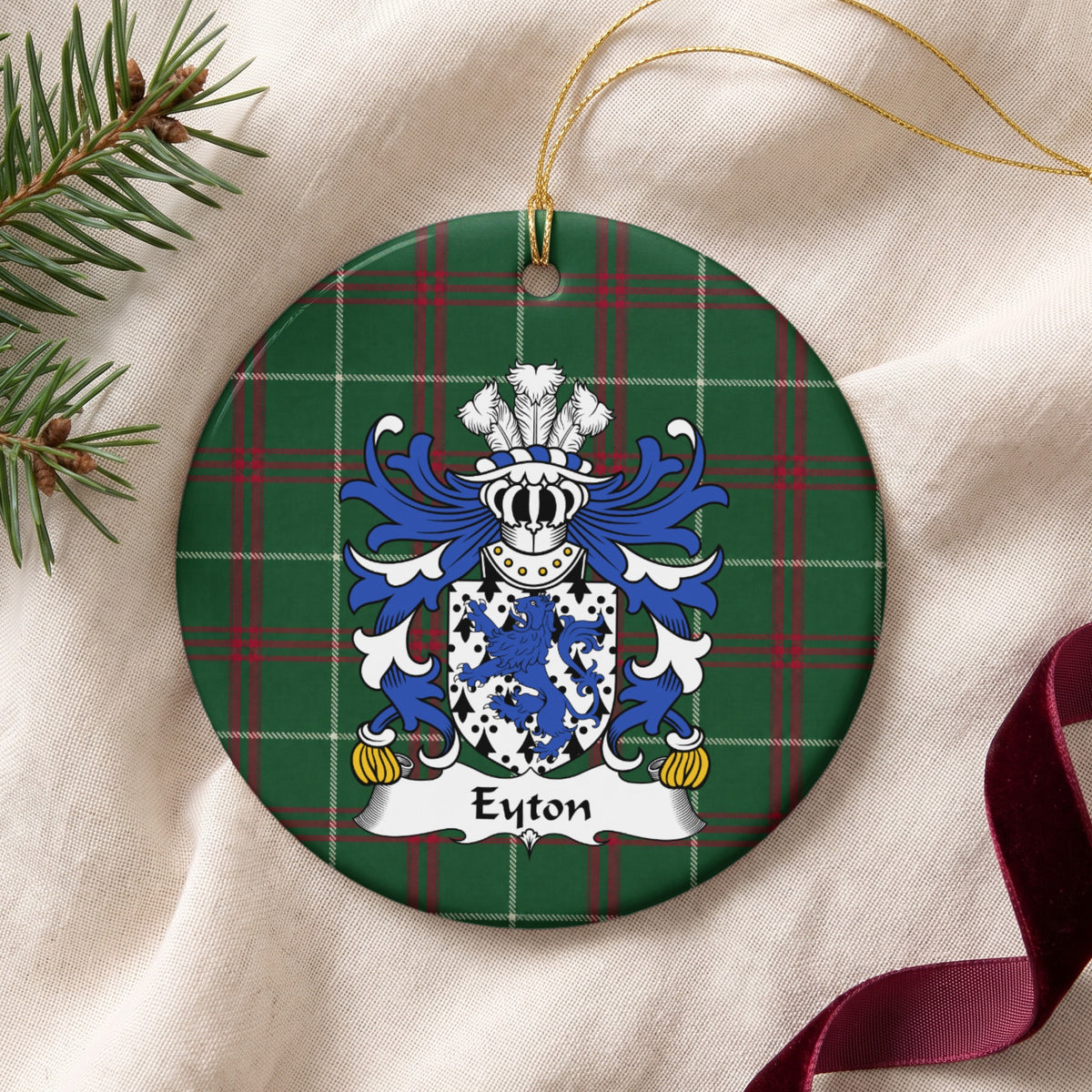 Eyton ornament on cream fabric beside evergreen and burgundy ribbon; a blue lion on a white shield patterned with black ermine marks on Welsh national tartan.
