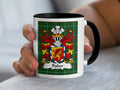 Mug with Fisher coat of arms on green plaid background, held by a hand.