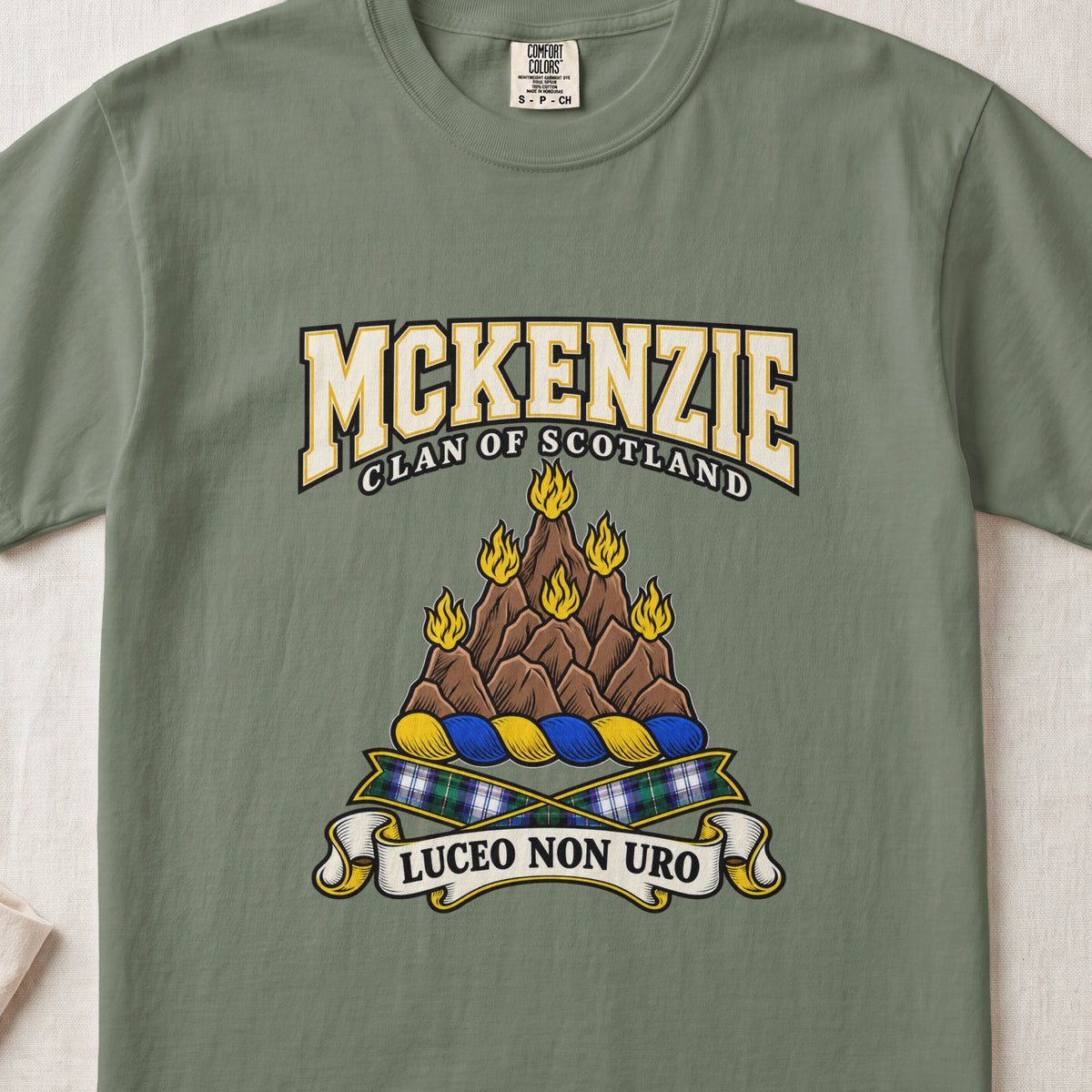 McKenzie graphic T-shirt in Moss green, front flat lay showing varsity lettering and brown rocky mountain-like mound with yellow flames.