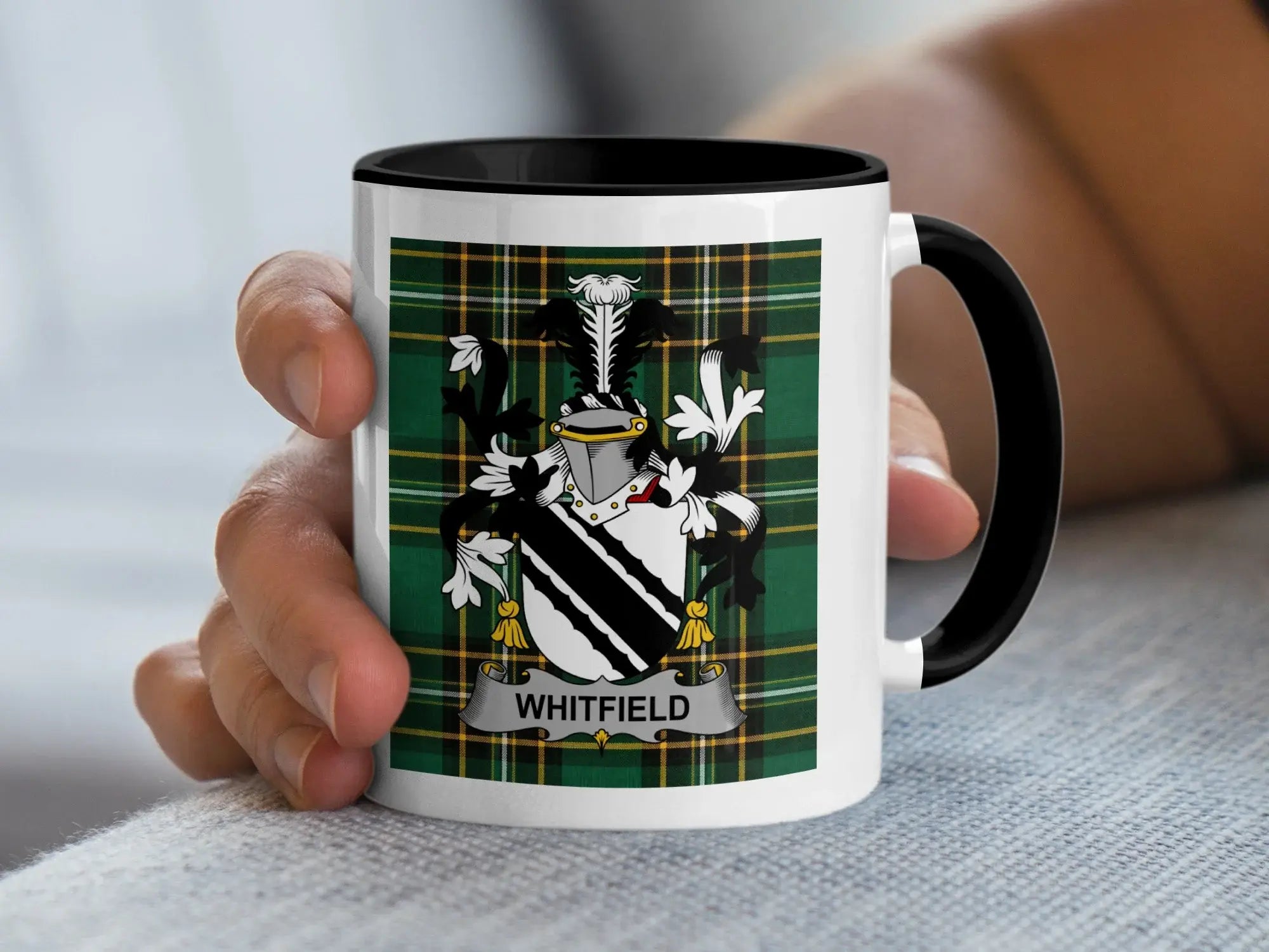 White mug with black rim featuring the Whitfield family crest on a plaid background.