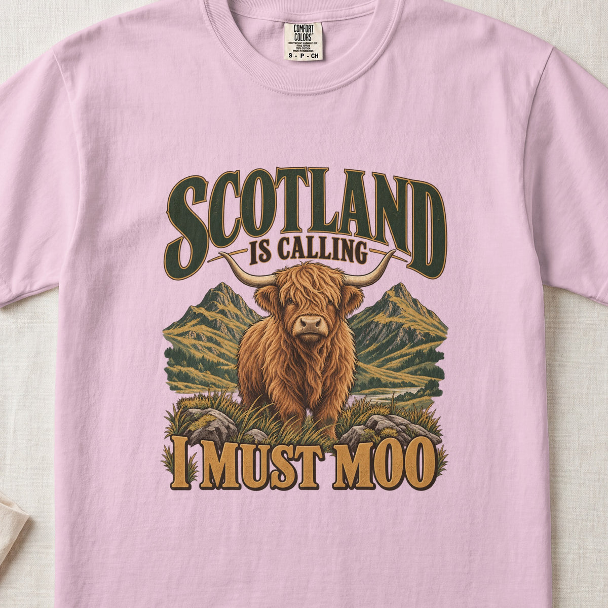 Scotland Is Calling, I Must Moo Highland cow design on a Blossom Comfort Colors 1717 T-shirt, flat lay