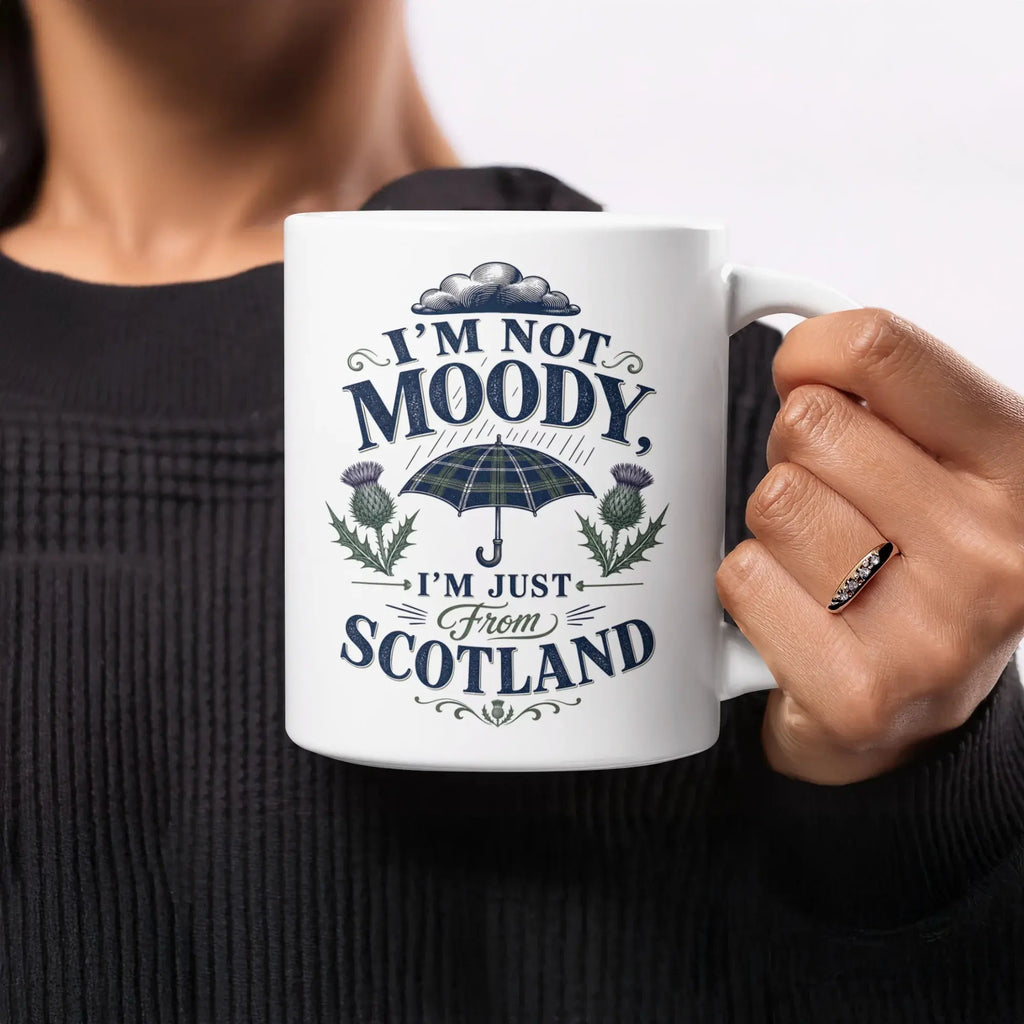 White mug with "I'm not moody, I'm just from Scotland" and tartan umbrella graphic.