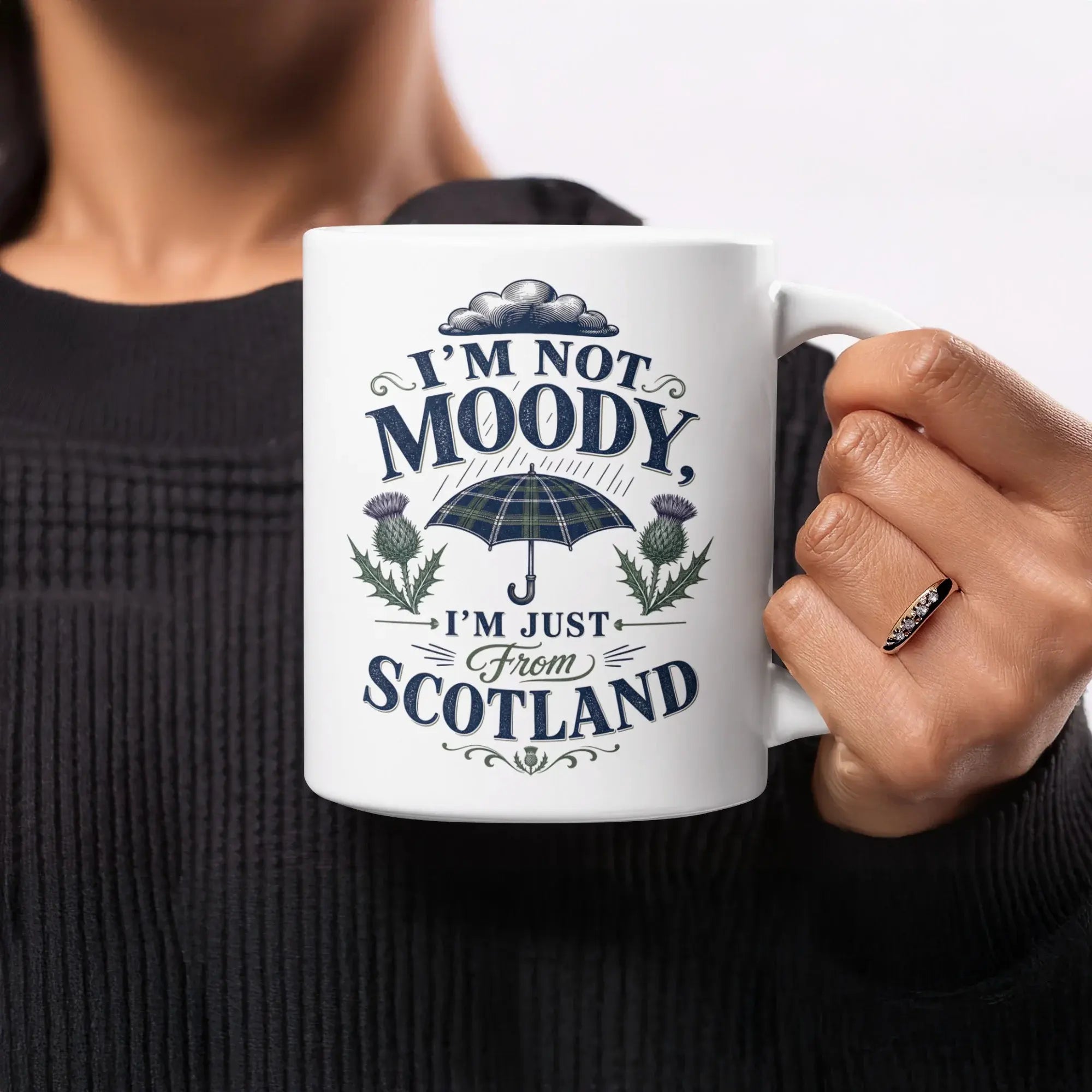 White mug with "I'm not moody, I'm just from Scotland" and tartan umbrella graphic.
