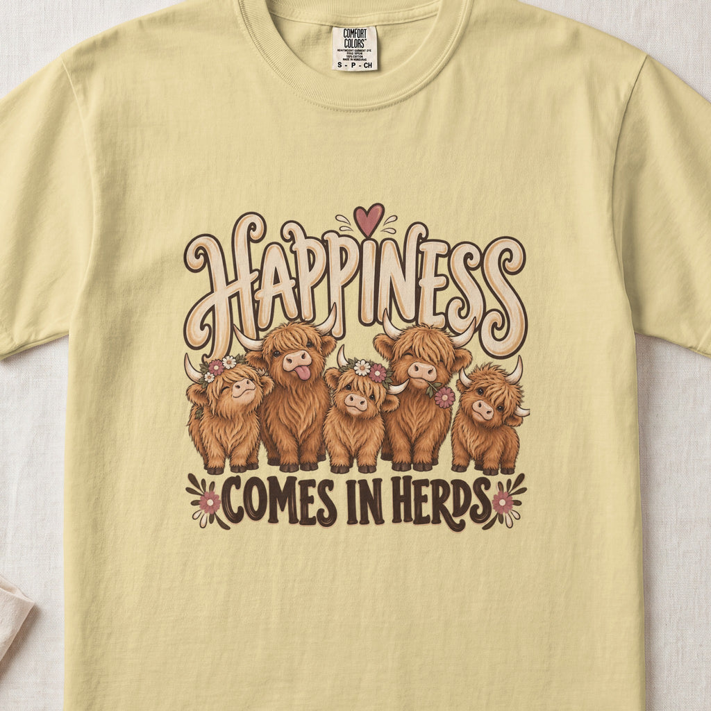 Happiness Comes in Herds Highland cow design on a Butter Comfort Colors 1717 T-shirt, flat lay