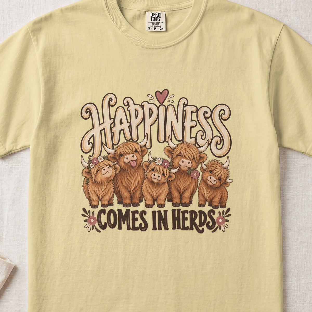 Happiness Comes in Herds Highland cow design on a Butter Comfort Colors 1717 T-shirt, flat lay
