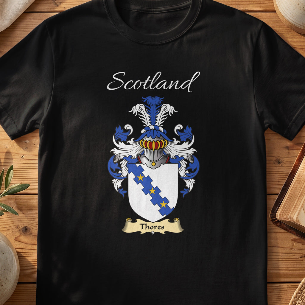 Black Thores Scottish family crest T-shirt laid flat, showing “Scotland” above a blue-and-silver shield crossed by stepped diagonal bands.