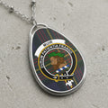 Silver oval pendant with Muir clan crest on tartan background with Latin motto.