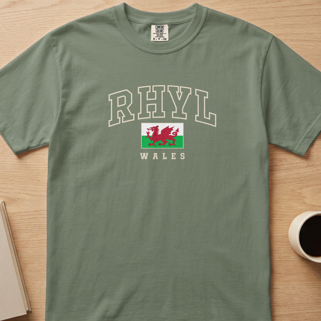 Moss green Rhyl Wales T-shirt laid flat, with cream collegiate outline lettering and a red Welsh dragon flag.