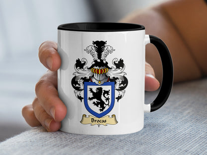 White mug with black rim and handle, featuring the Brocas family crest.