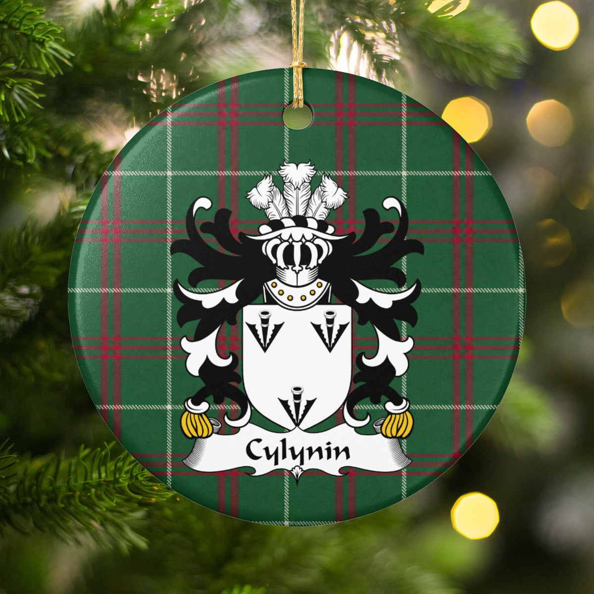 Cylynin ornament hanging among Christmas tree branches and warm lights; three black arrowhead motifs on a white shield on Welsh national tartan.