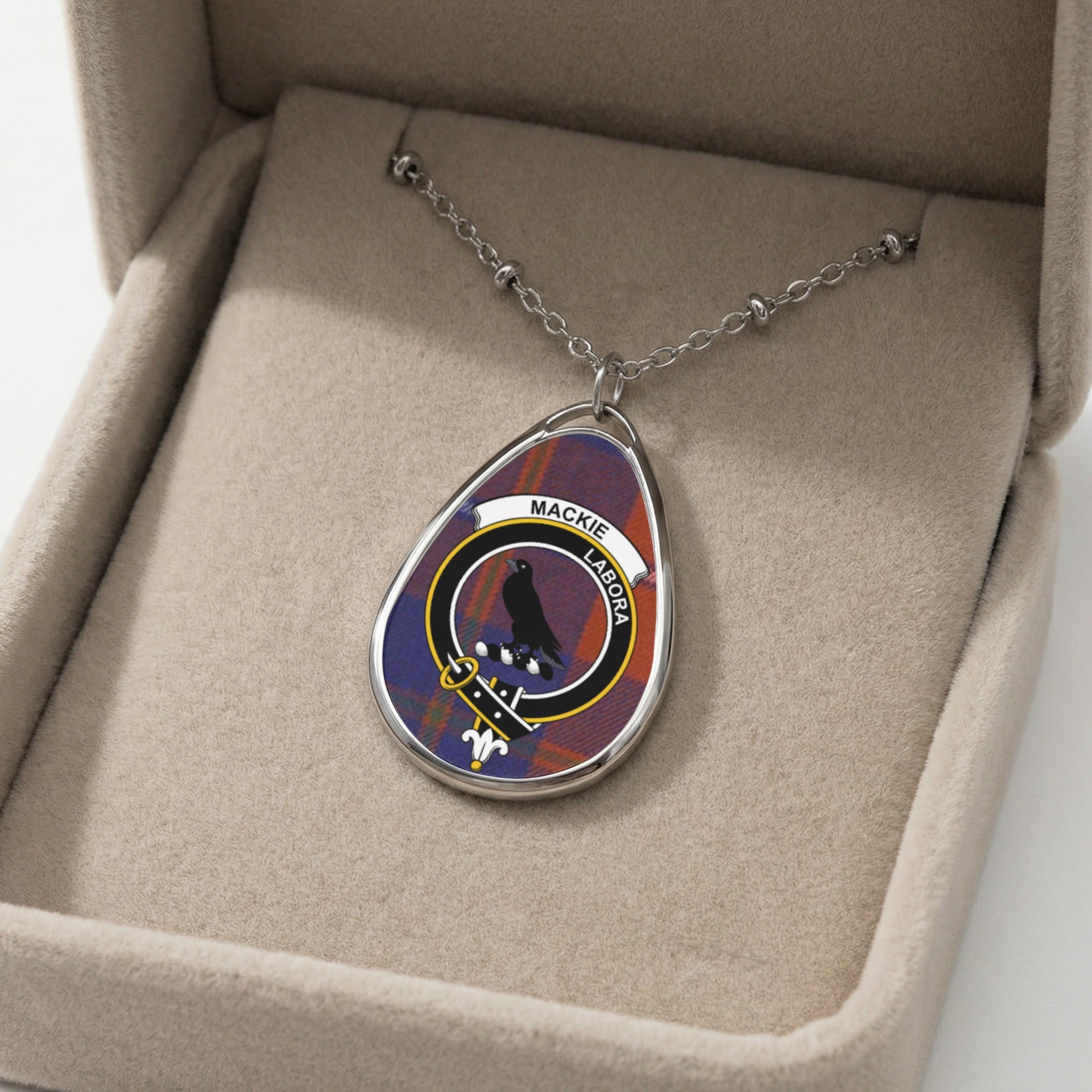 Mackie crest pendant necklace on tartan background in a display box.