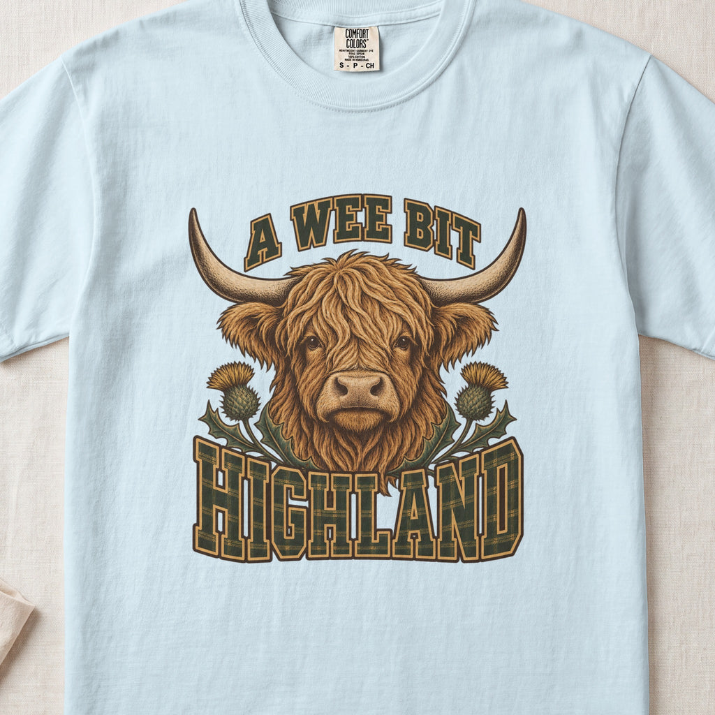 A Wee Bit Highland Highland cow design on a Chambray Comfort Colors 1717 T-shirt, flat lay
