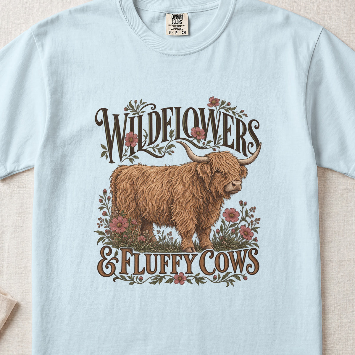 Wildflowers & Fluffy Cows Highland cow design on a Chambray Comfort Colors 1717 T-shirt, flat lay