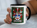 Mug with Trench family crest and plaid pattern held by a hand.