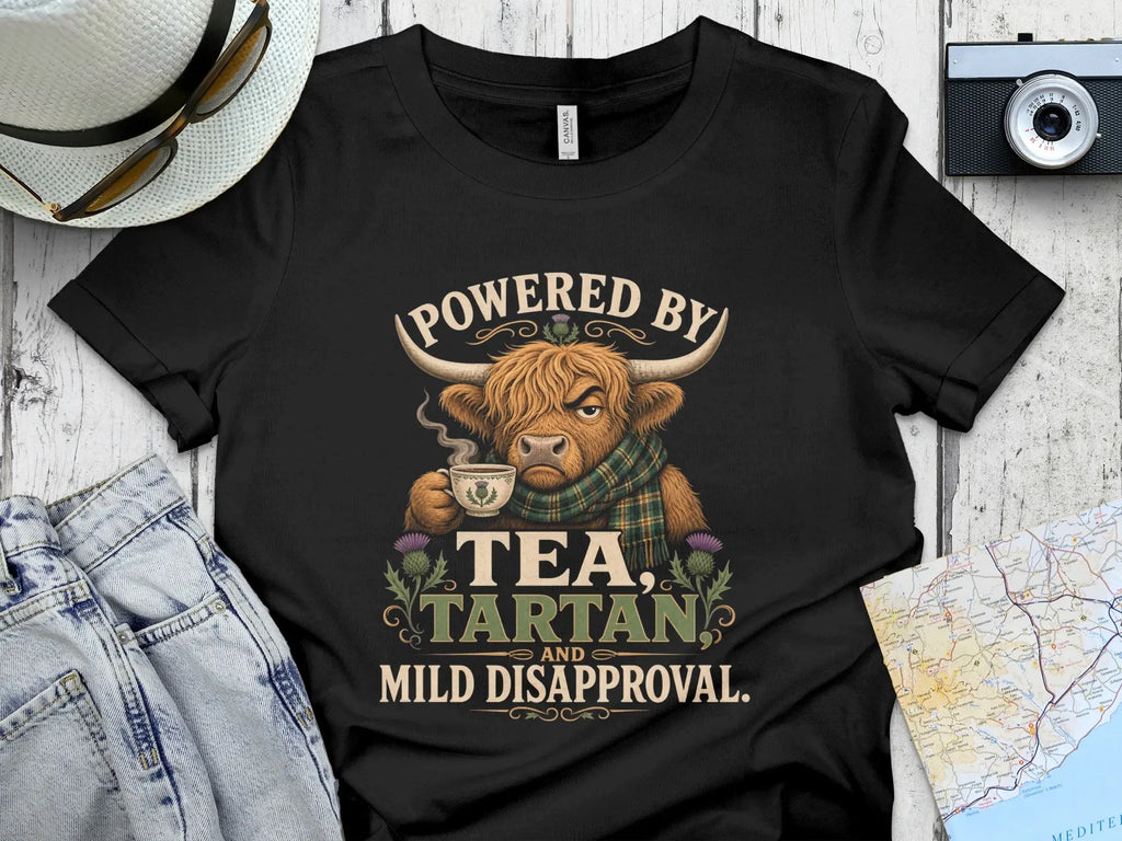T-shirt with Highland cow drinking tea, "Powered by Tea, Tartan and Mild Disapproval."