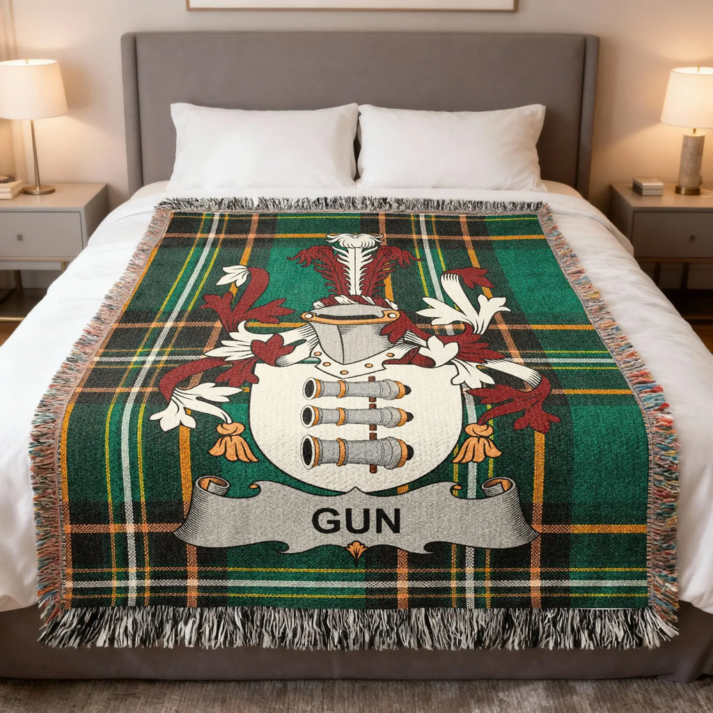 Tartan blanket with crest and "GUN" text draped on a bed.