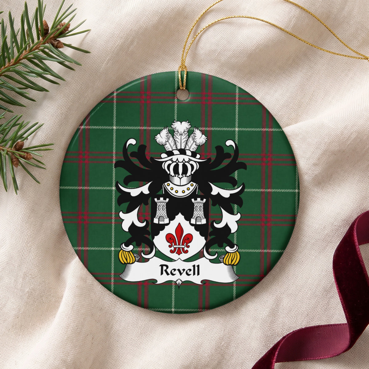 Revell ornament on cream fabric beside evergreen and burgundy ribbon, with two silver towers above a red fleur-de-lis on a black and white shield.