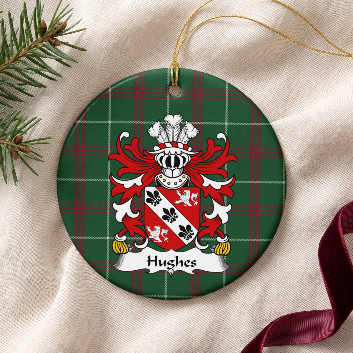 Hughes Style 4 ornament on cream fabric with gold string, evergreen and burgundy ribbon; a white diagonal band with black fleurs-de-lis between two white lions on a red shield on Welsh national tartan.